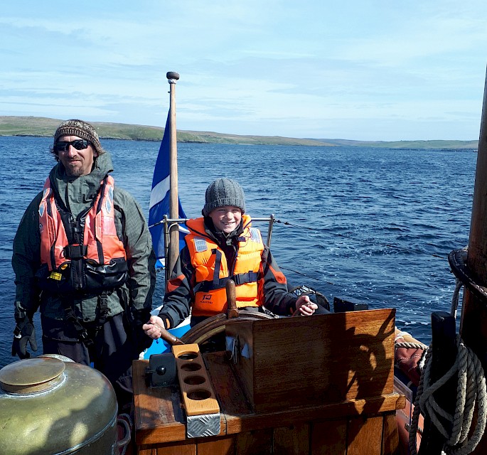 School pupil enjoys his turn at the helm, under the watchful eye of Swan Skipper Thorben Reinhardt