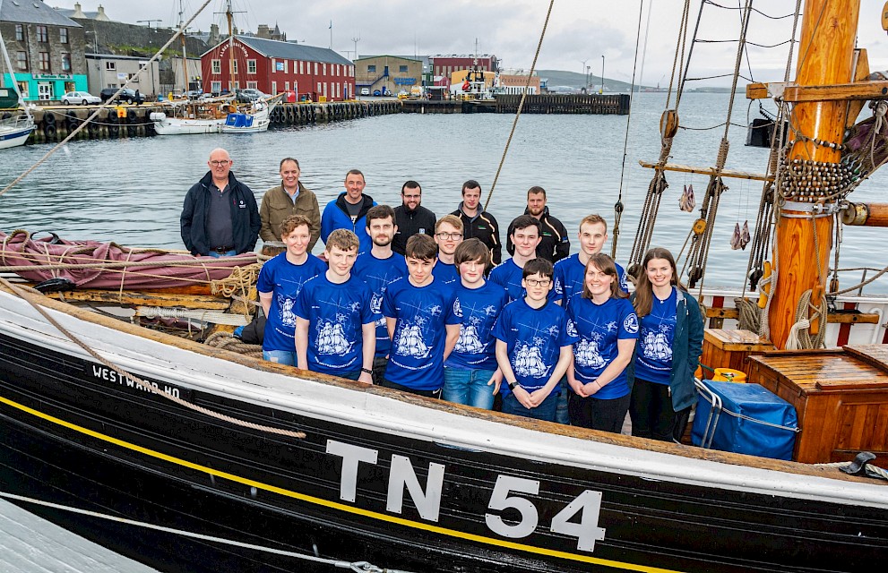 Sail Training Shetland sail trainees and sponsors pictured on board Faroese sailing smack Westward Ho at Victoria Pier North Pontoons. Back Row (L to R) Sponsors, David Goodlad - Mørenot Aquaculture, John Henderson - Lerwick Port Authority, Richie Fraser - EnQuest on behalf of the Sullom Voe Terminal owners, Steven Hutton - J.R. Hutton Consulting Ltd, Peter & Joe Smith - Tulloch Developments Ltd. Middle Row (L to R) Sail Trainees – Abi Marples (21) Lerwick, Andrew Manson (23) Brae, Daniel Sinclair (18) Cunningsburgh, Malachi Hendry (16) Cunningsburgh, Michael Noblett (21) Lerwick, Ailish Parham - Sail Training Shetland. Front Row (L to R) Sail Trainees – James Phillips (16) Lerwick, Jay Milne (15) Lerwick, Xenon Johnson (15) Lerwick, Aaron Regler (15) Lerwick, Sarah Kissick (21) South Nesting and Ailish Parham – Sail Training Shetland. Missing from photo - Laura Bowles (15) Walls and Jan Peters (17) Orkney. Photo Credit – Gordon Siegel Photography