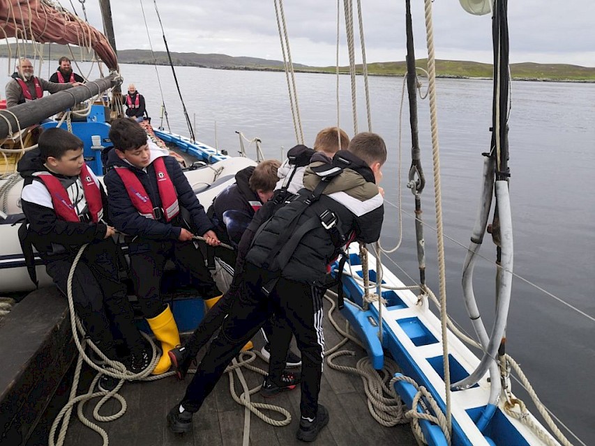 Heave ho! Pupils haul the gaff and boom into the boom crutch on deck.