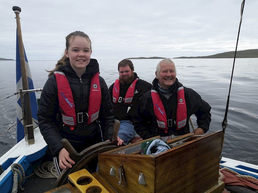 One of the Whalsay school pupils takes the helm, under the supervision of long standing volunteer crew member Ian Nicolson and Swan Skipper Scott Sandison