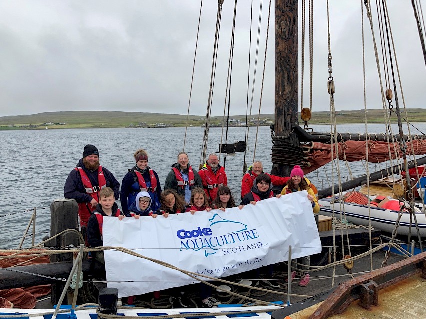 Baltasound Secondary 1 pupils holding the sponsor banner, with school staff and Swan crew