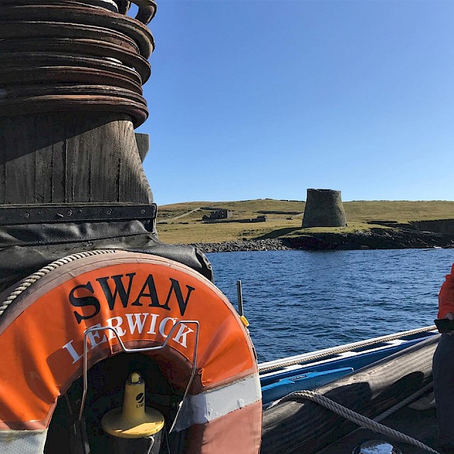 The Swan anchored off Mousa, with a view to the Iron Age Broch