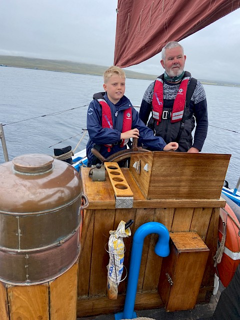 Baltasound school pupil takes the helm, with volunteer crew member Peter Robertson